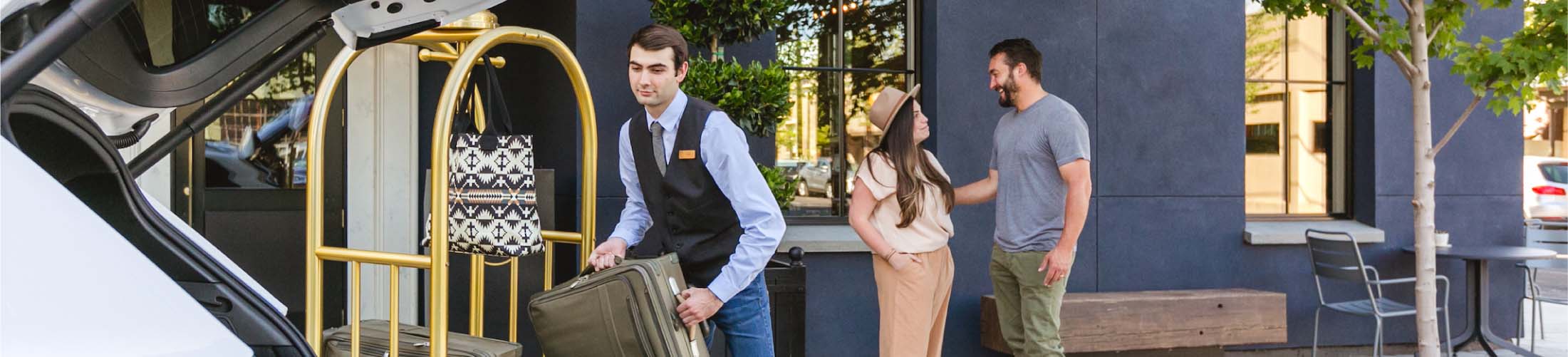An Atticus Hotel valet loads luggage onto a cart for a couple standing behind him.