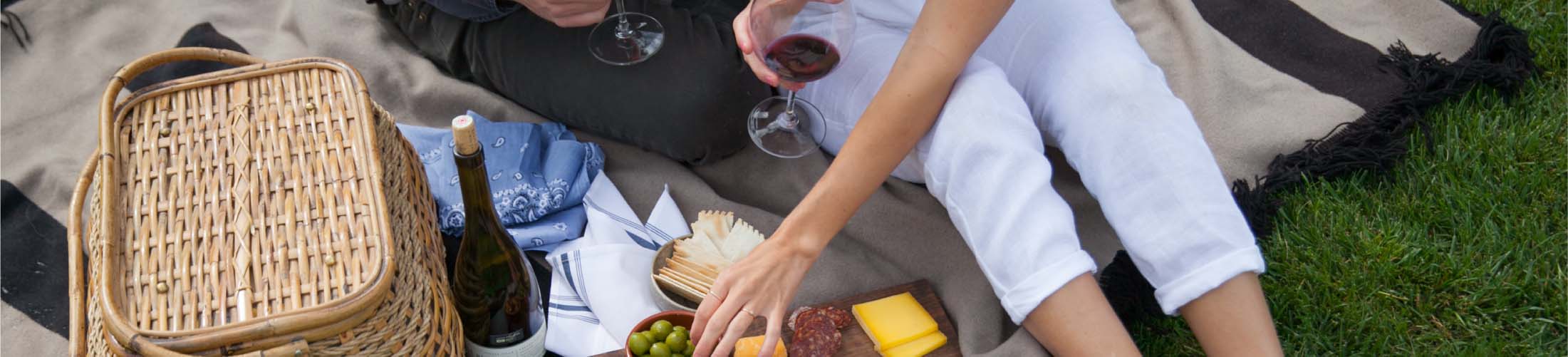 A picnic basket, bottle of wine and charcuterie board.
