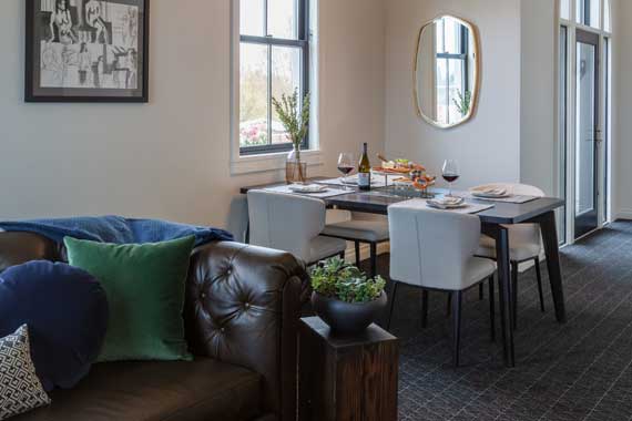 Cozy living and dining area with a tufted brown leather sofa, colorful cushions, and a dining table set near the window.